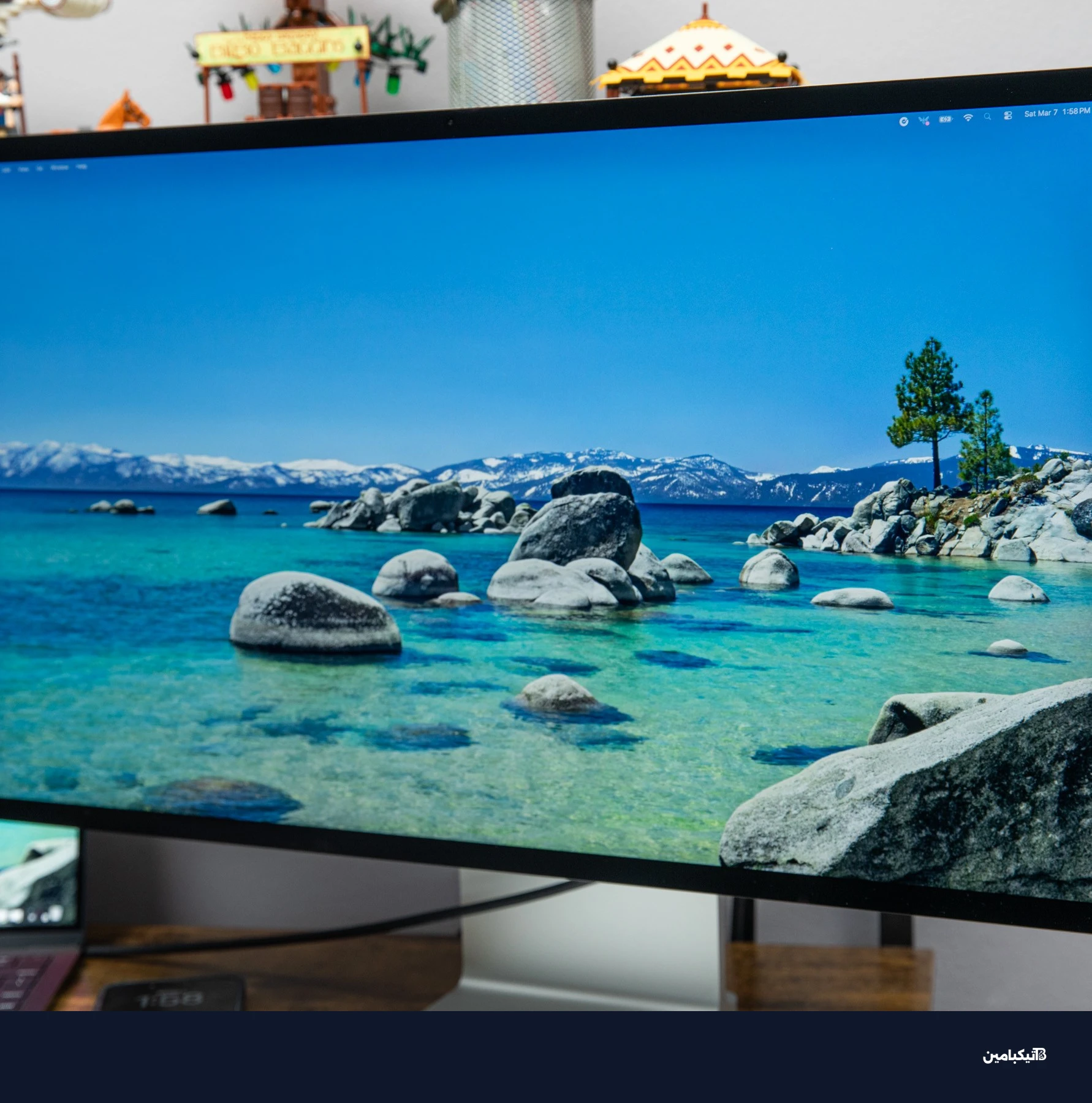 شاشة آبل Studio Display XDR تعرض منظر طبيعي مائي على مكتب خشبي بجوار جهاز ماك بوك.