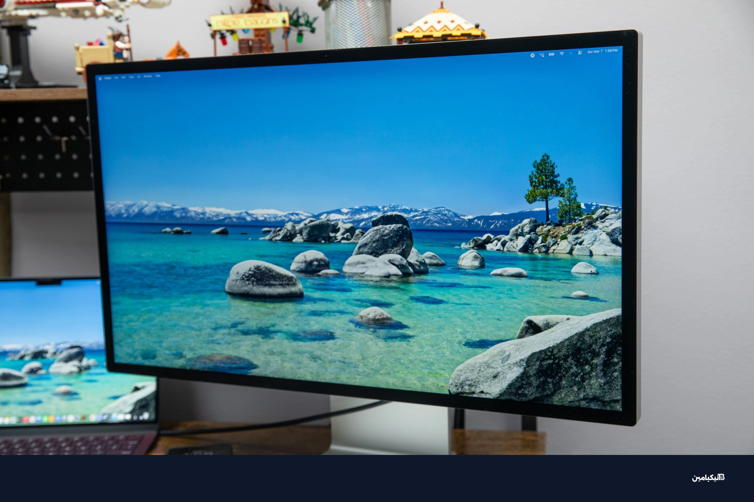 شاشة آبل Studio Display XDR تعرض منظر طبيعي مائي على مكتب خشبي بجوار جهاز ماك بوك.