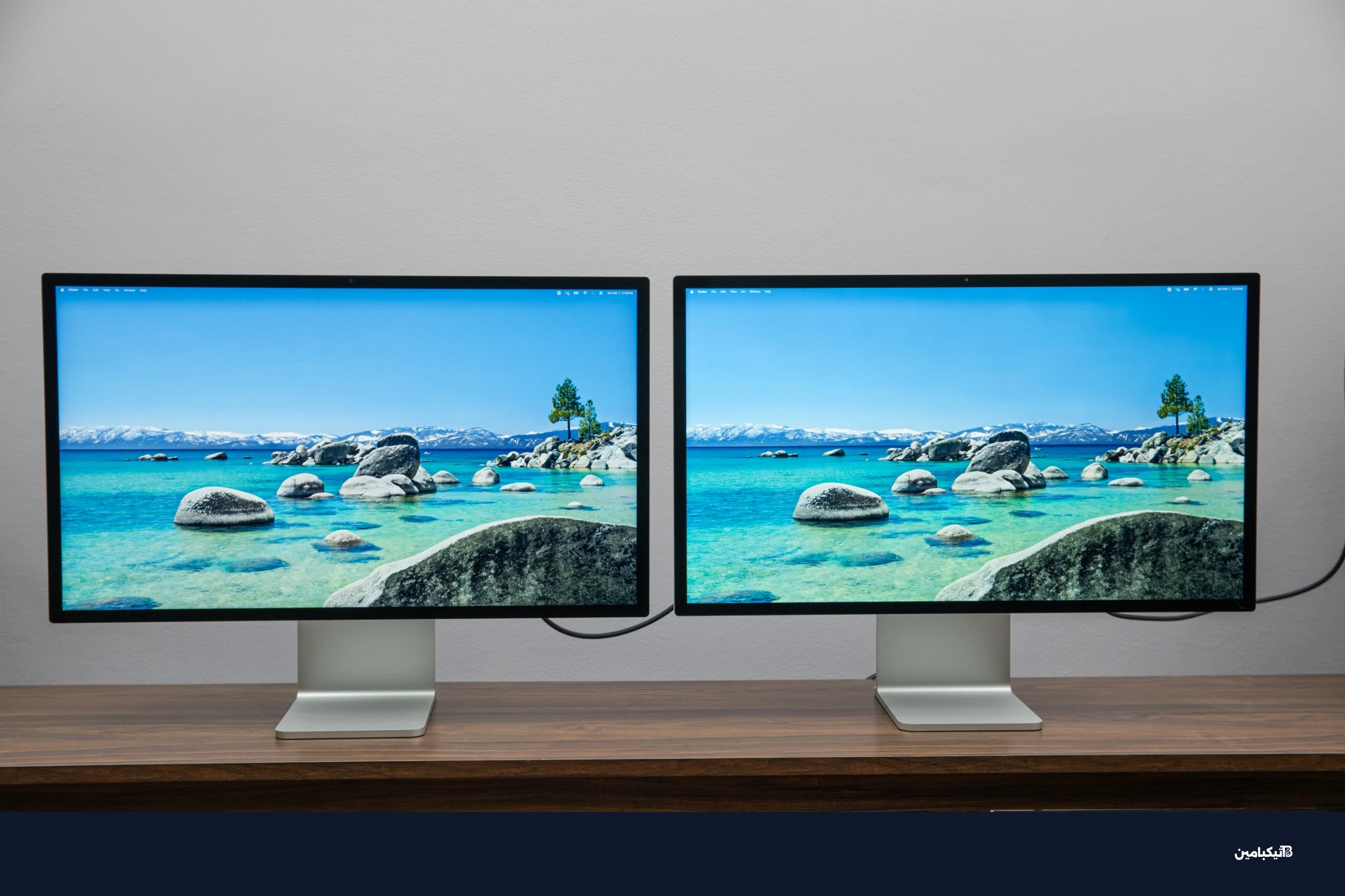 شاشة آبل Studio Display XDR وشاشة Studio Display جنباً إلى جنب على طاولة خشبية.