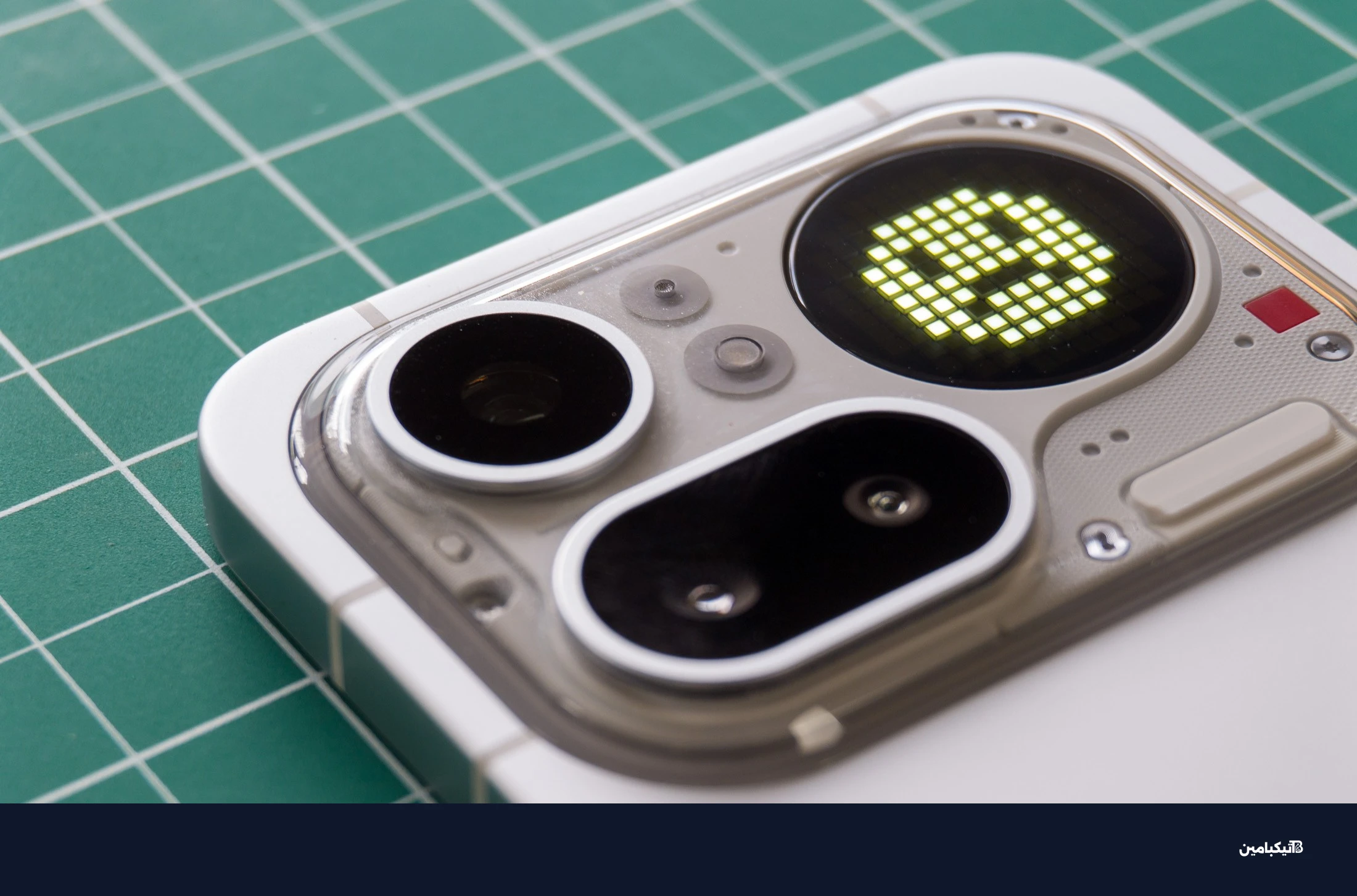 صورة لهاتف Nothing Phone 4A Pro على حصيرة خضراء تظهر وحدة الكاميرا مع وجه ابتسامة غير سعيدة على شاشة Glyph Matrix