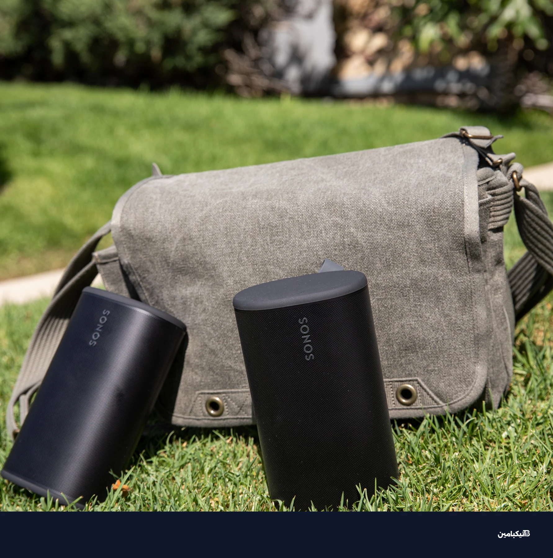 Two Sonos Play speakers in front of a sage colored bag on the grass.